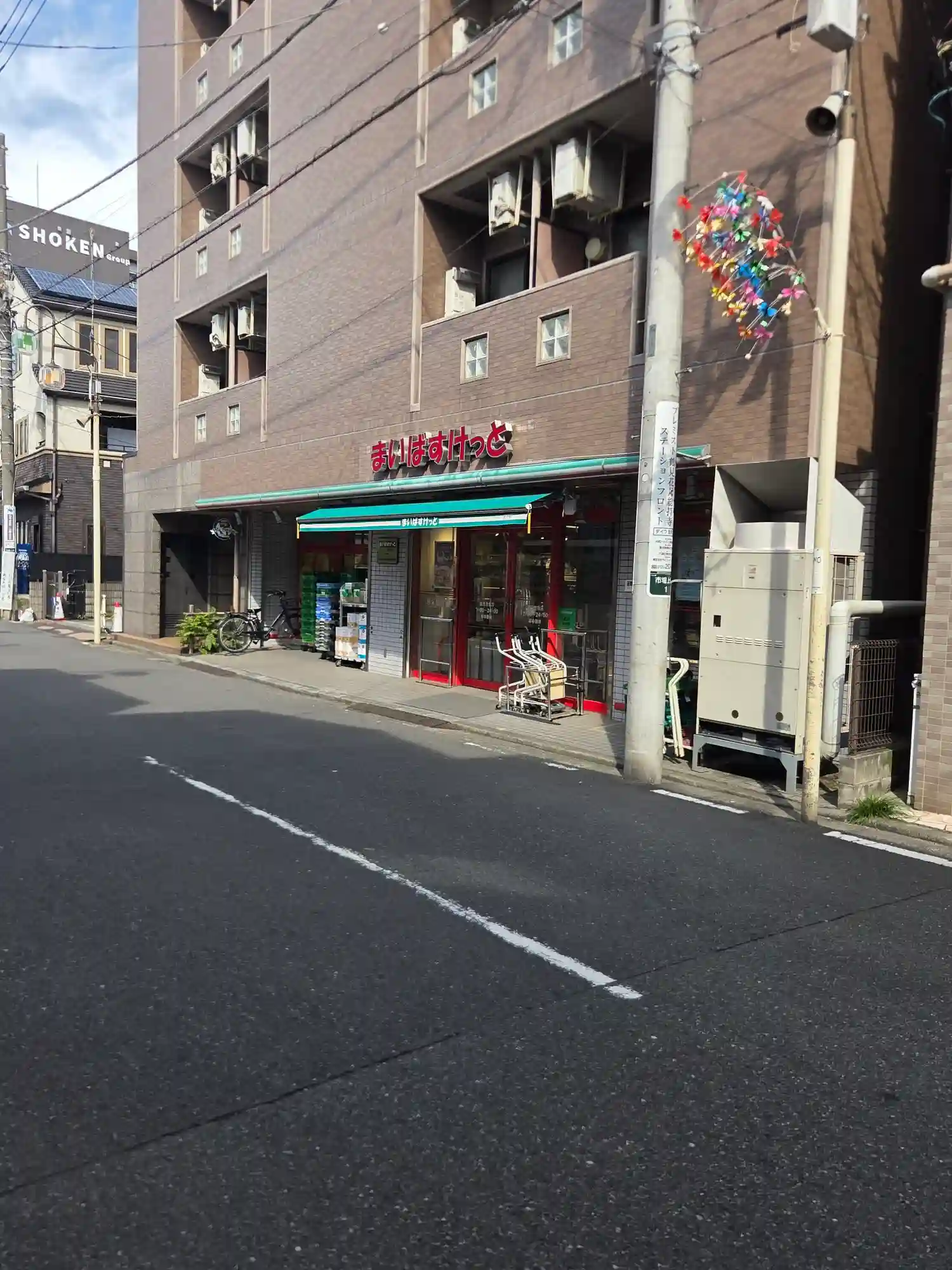 鶴見市場駅近くのまいばすけっとの外観。マンション1階に入る小型スーパーで、店頭に買い物カートと商品棚が並ぶ