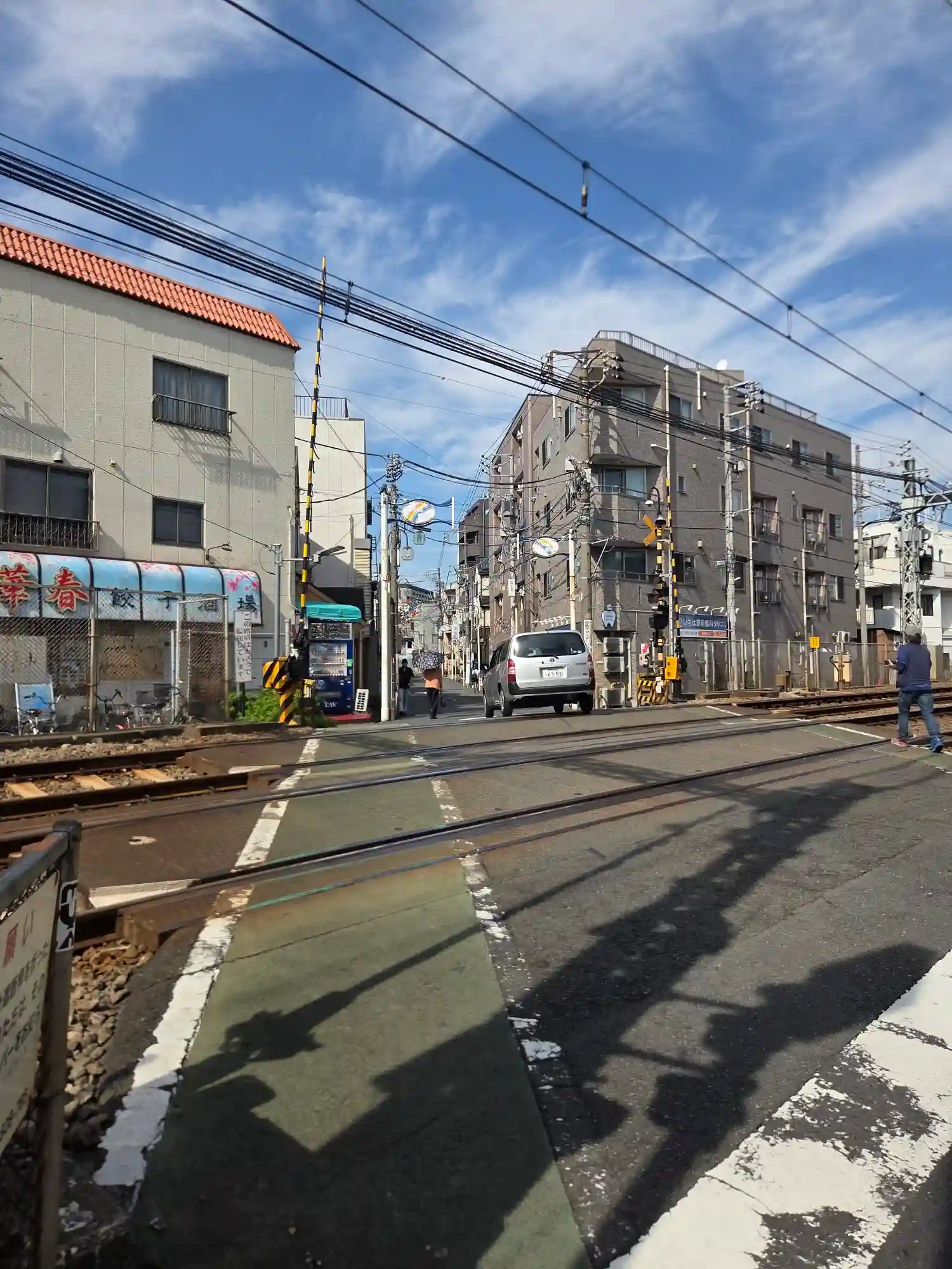鶴見市場駅横の踏切から見た駅前通り。線路沿いに飲食店や商店が並び、中低層の建物が続く街並み