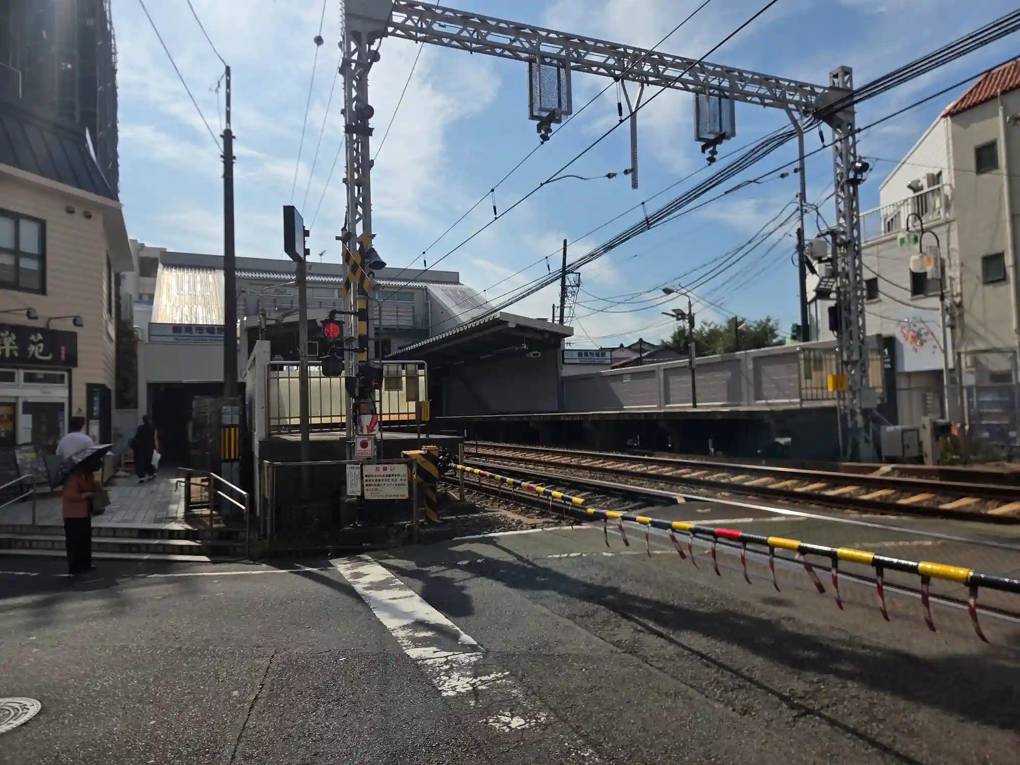 踏切から見た鶴見市場駅のホームと駅舎。京急本線の線路が地上を走り、駅のすぐ横に踏切がある