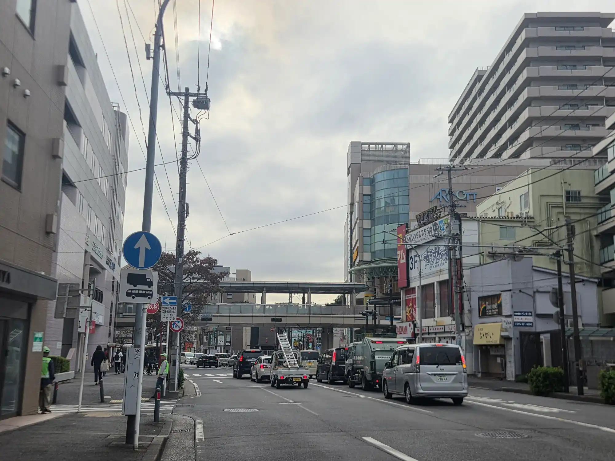 二俣川駅北口の駅前通り。ペデストリアンデッキの手前にアルコット二俣川やカラオケ店、飲食店が並び、平日夕方も車と人の通りがある