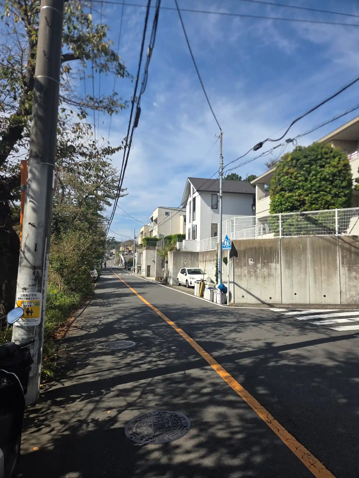 白楽駅周辺の住宅街の上り坂。擁壁の上に一戸建てやマンションが建ち、坂の多い白楽の地形がわかる道路