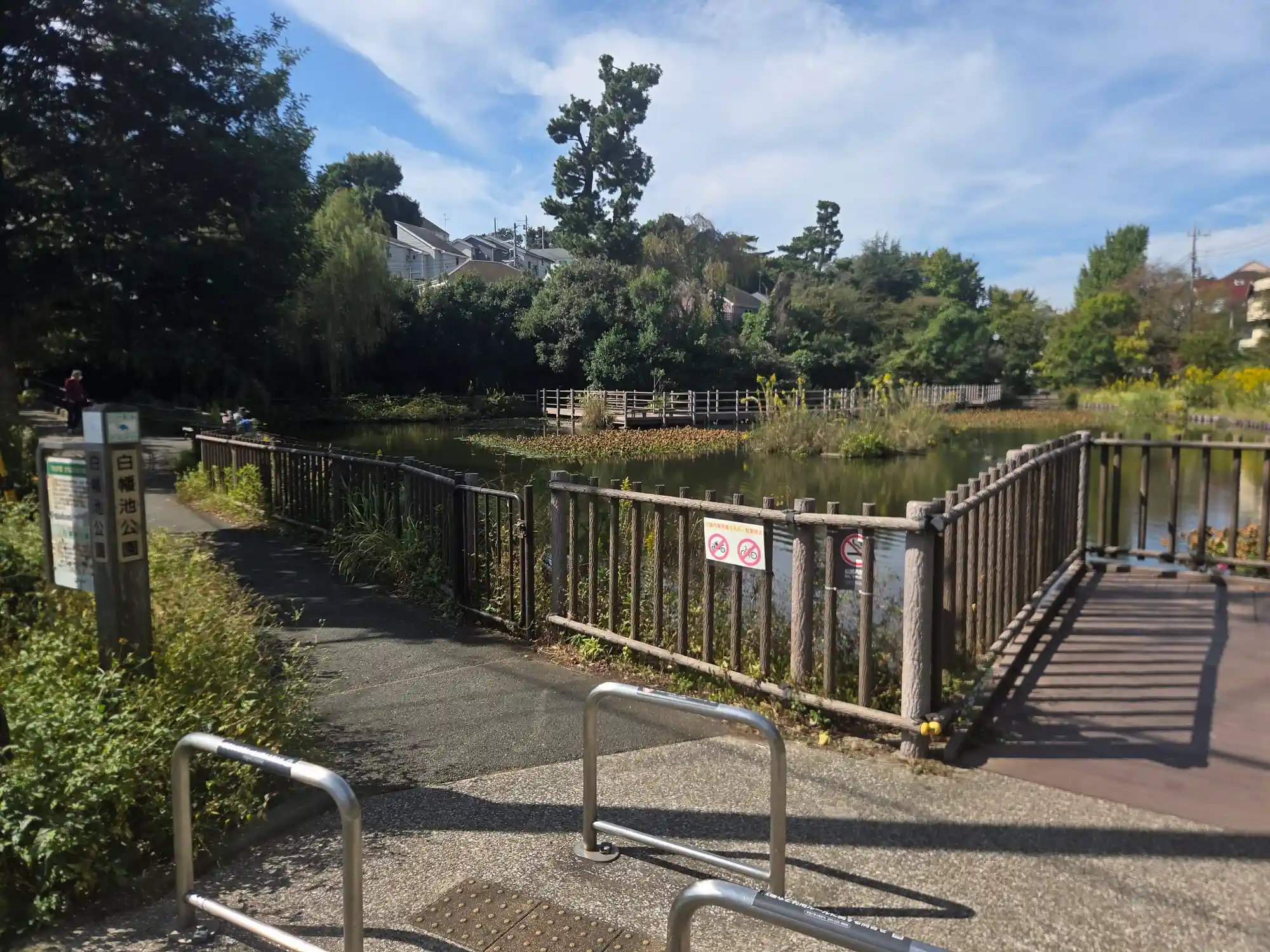白楽駅周辺にある白幡池公園の入口。公園名の看板の先に池と木製の柵が続き、奥に住宅街が見える