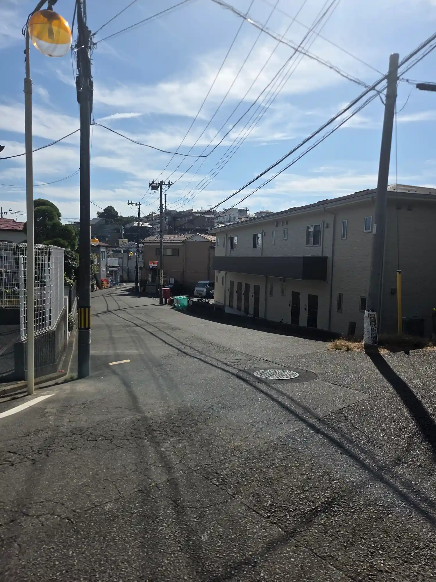 白楽駅周辺の下り坂に建つ2階建てのアパート。奥の丘にも住宅が重なって見え、高低差のある白楽の地形がわかる