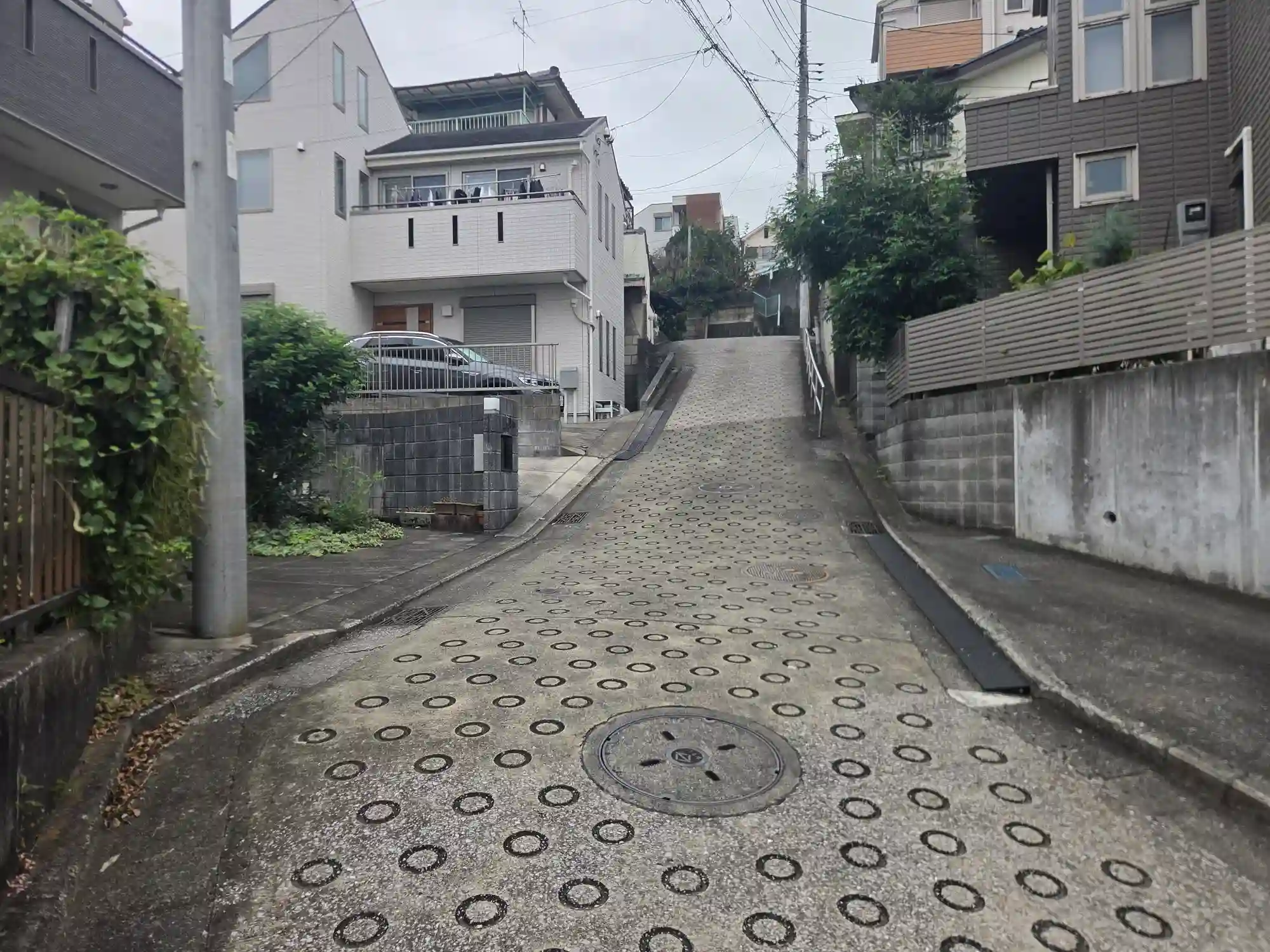 二俣川の住宅街にある急な坂道。路面には丸い溝の滑り止め舗装が施され、手すりの付いた坂が丘の上の住宅まで続く