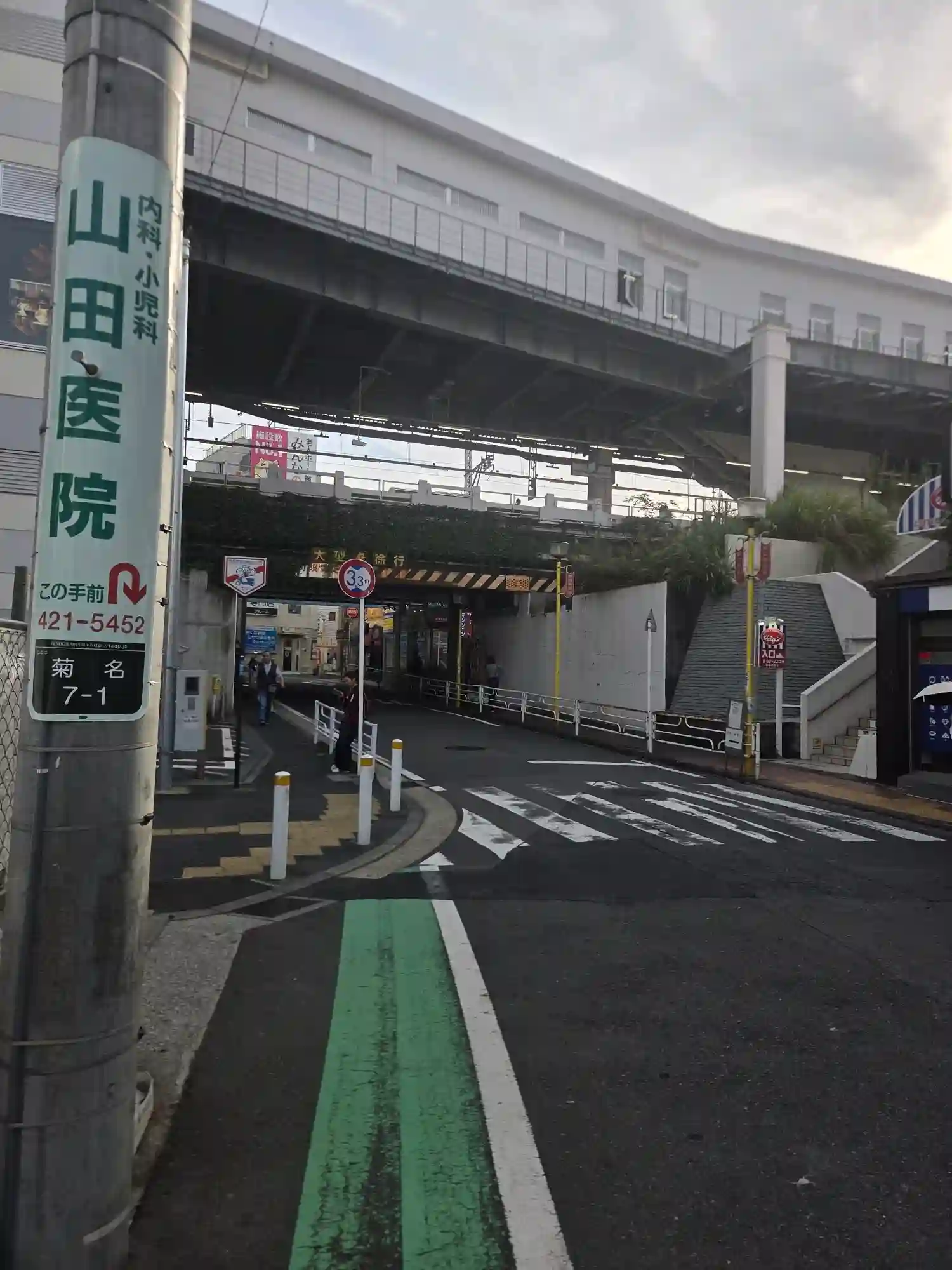 菊名駅前の高架下の道路。高さ制限3.3mの標識があり、道幅が狭く車と歩行者が近い様子