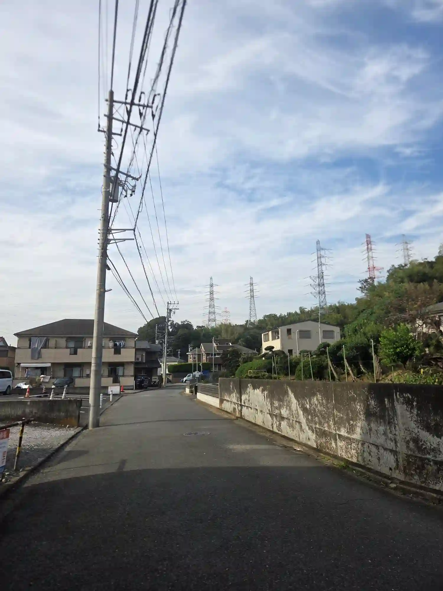 大倉山の住宅街の道。アパートと戸建てが並び、丘の上に送電鉄塔が見える