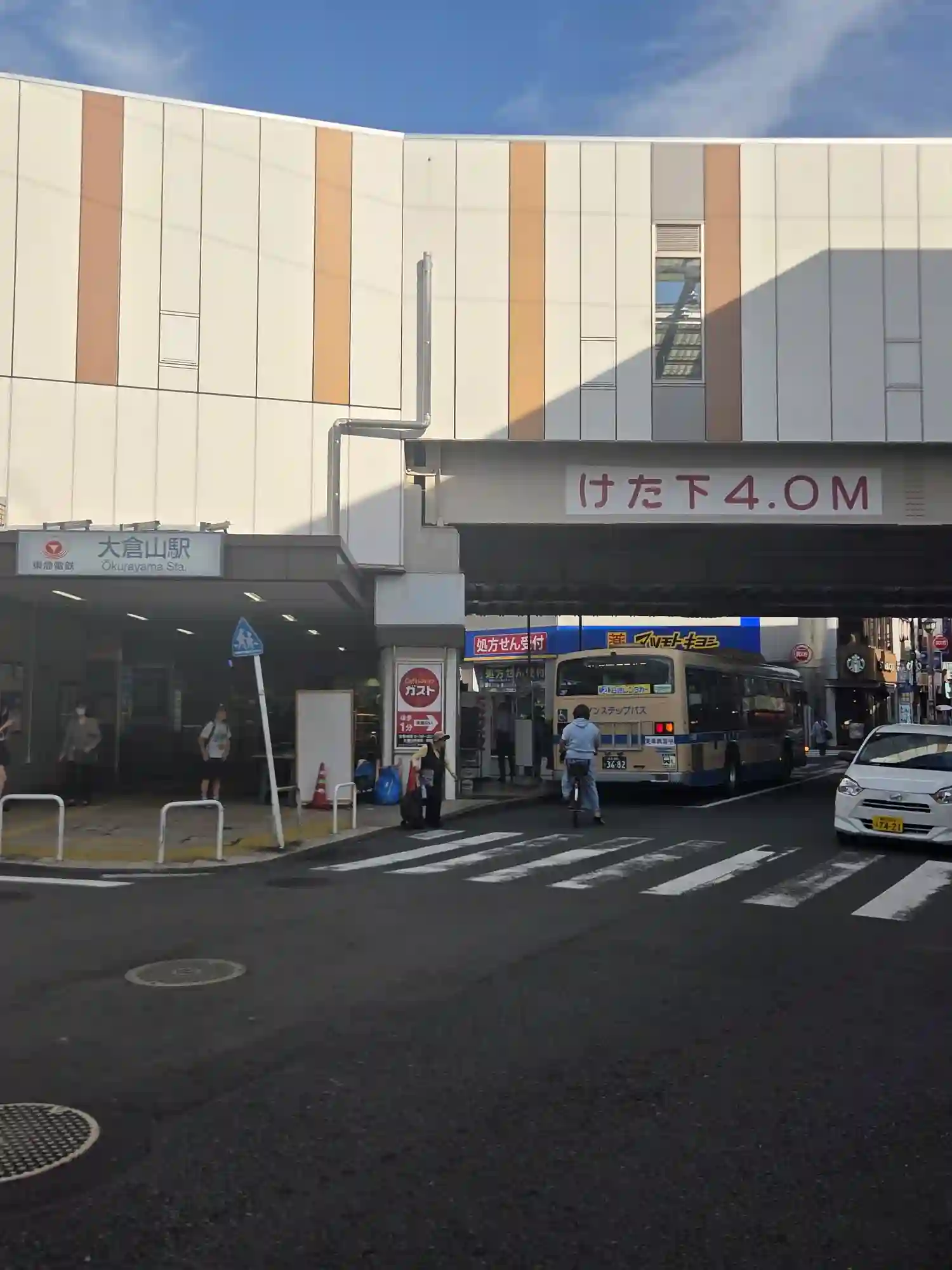 東急東横線大倉山駅の駅舎と駅前の横断歩道。高架下を路線バスが通る