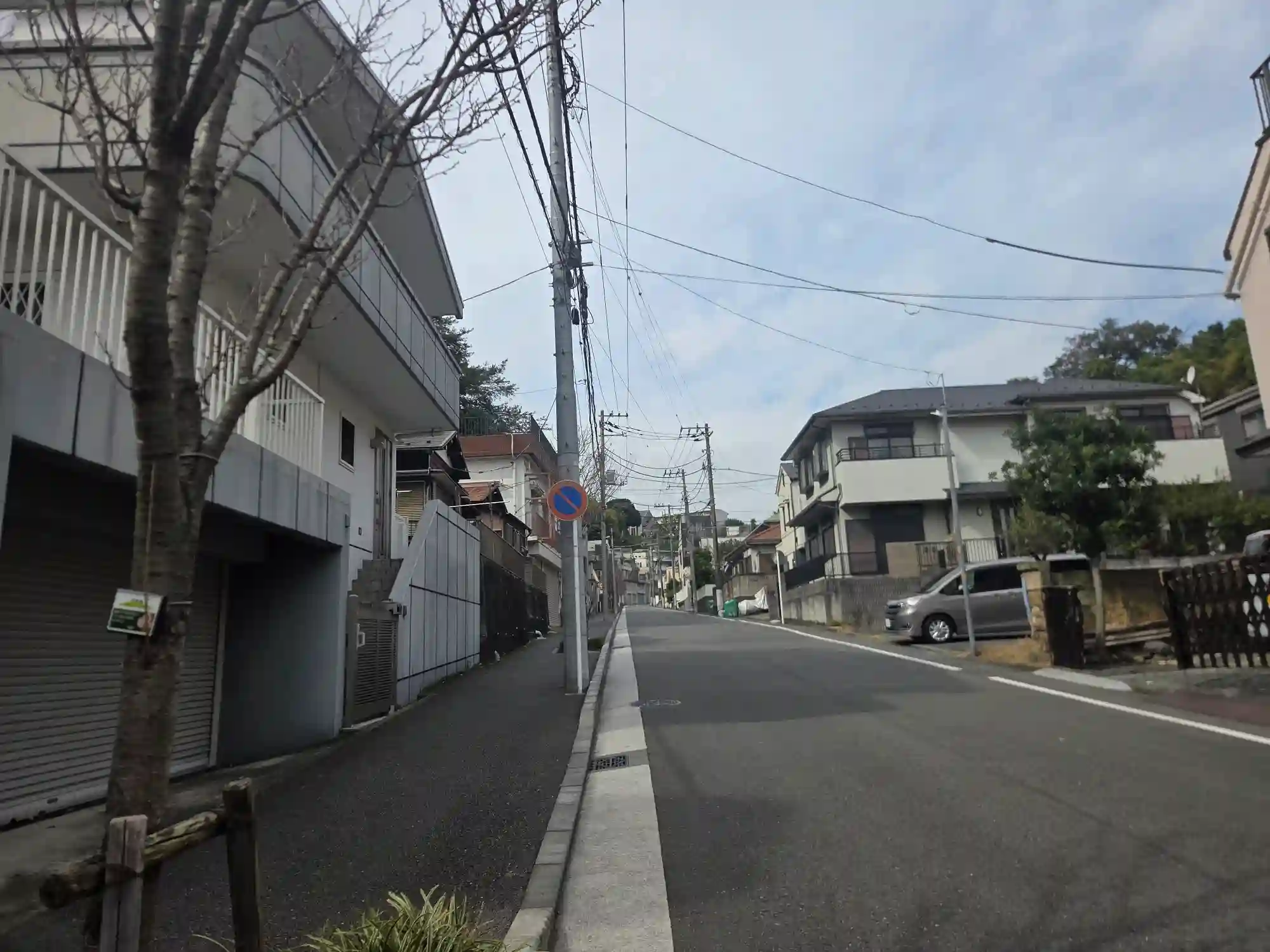 保土ヶ谷の丘に広がる住宅街。上り坂の道の先に、斜面に沿って家が段々に建ち並ぶ様子が見える