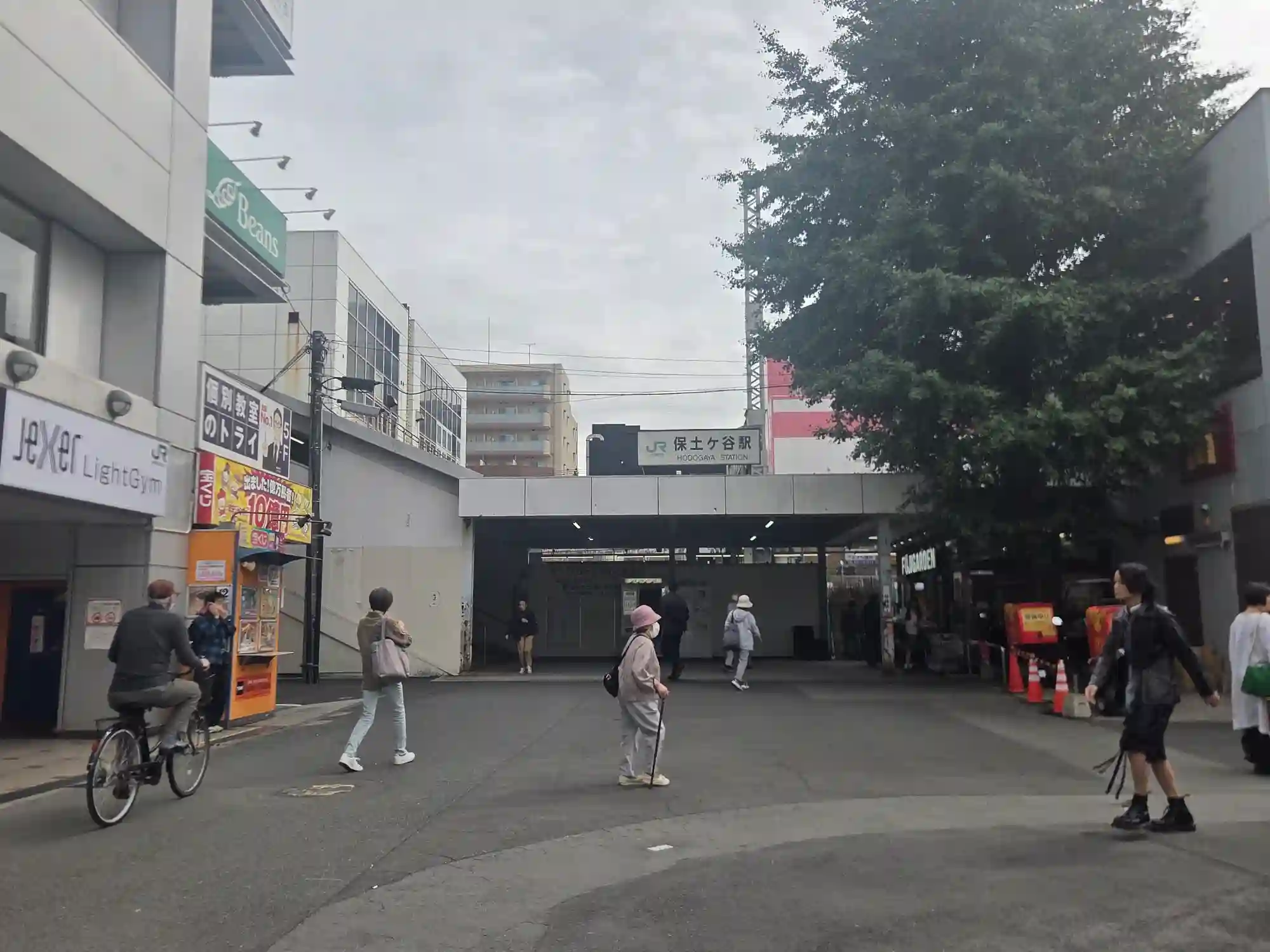 JR保土ヶ谷駅の入口と駅前広場。曇りの日中に、自転車や徒歩の人が行き交う落ち着いた雰囲気
