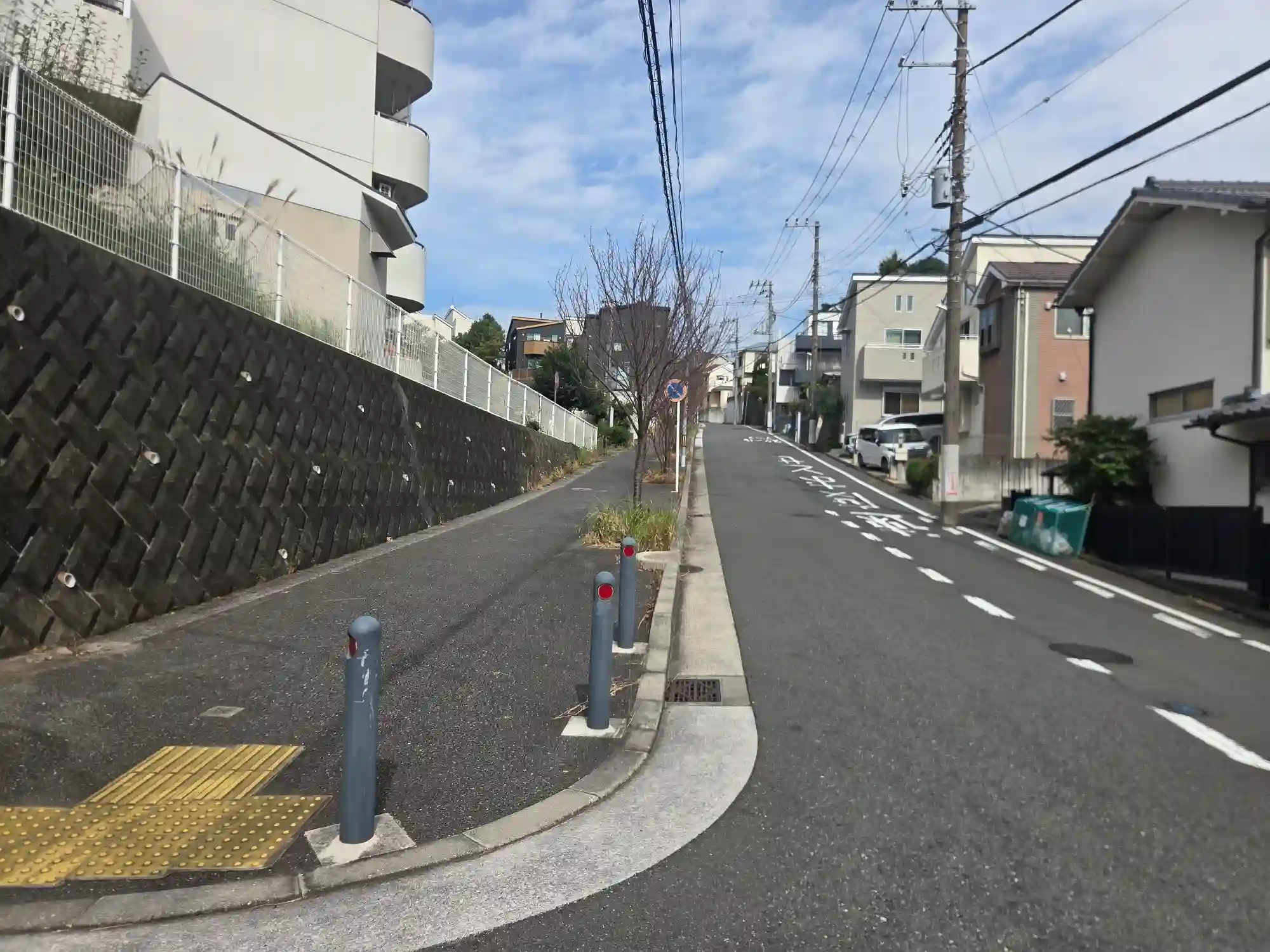 保土ヶ谷の住宅街にある上り坂。左側に高い擁壁が続き、坂の上にマンションや戸建てが建っている