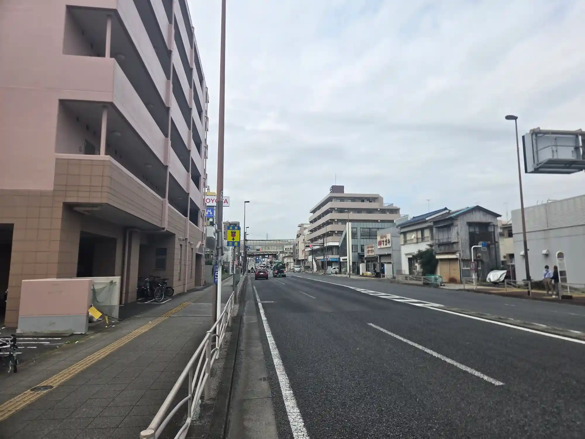 星川駅周辺の幹線道路沿いに並ぶマンションと商店。道路は広く平坦で、奥に相鉄線の高架が見える