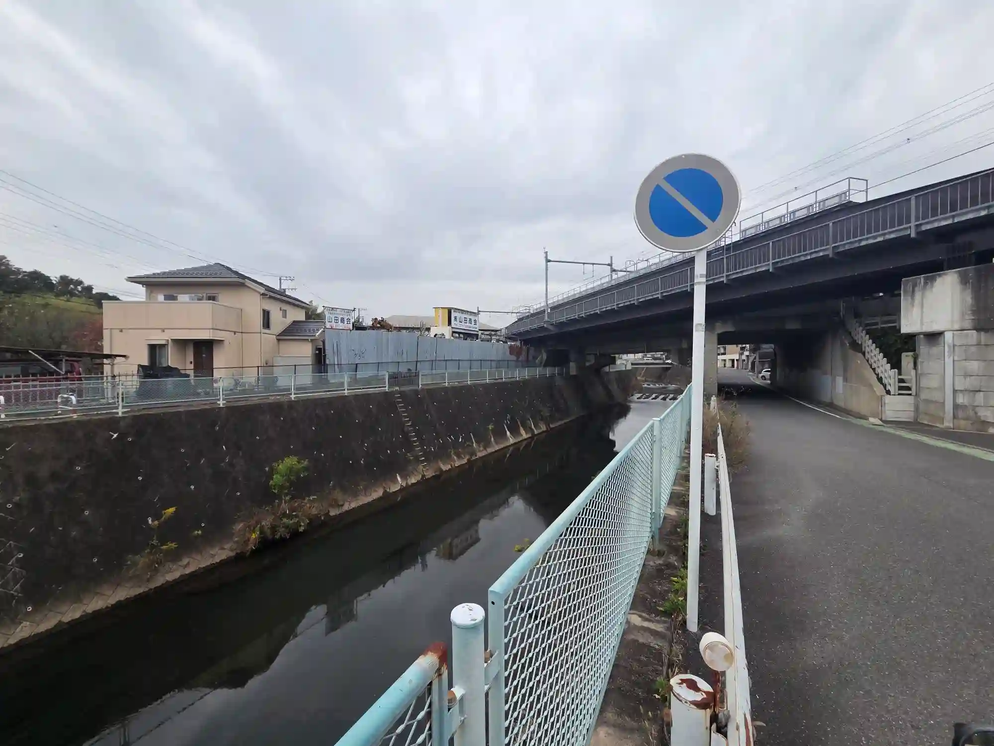 西谷駅周辺の川沿いの道。川の真上を線路の高架が通り、低地に住宅と道路が集まっている