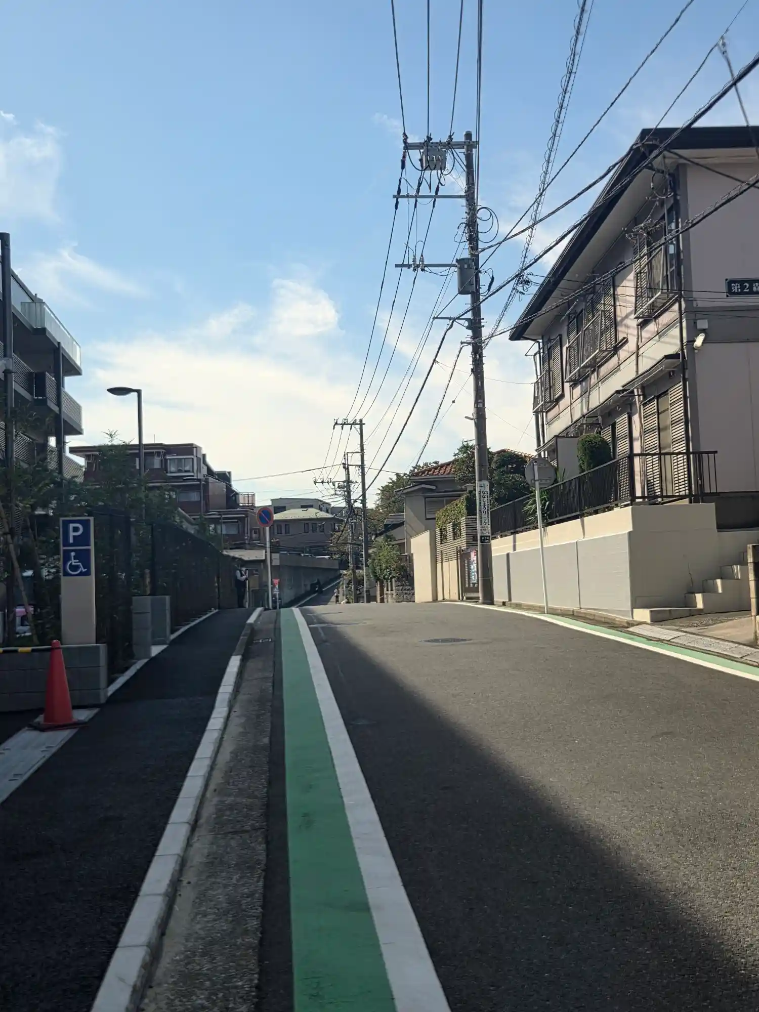 新子安駅周辺の住宅街に続く上り坂。自転車レーンのある道の両側にマンションとアパートが並び、奥に行くほど高くなる