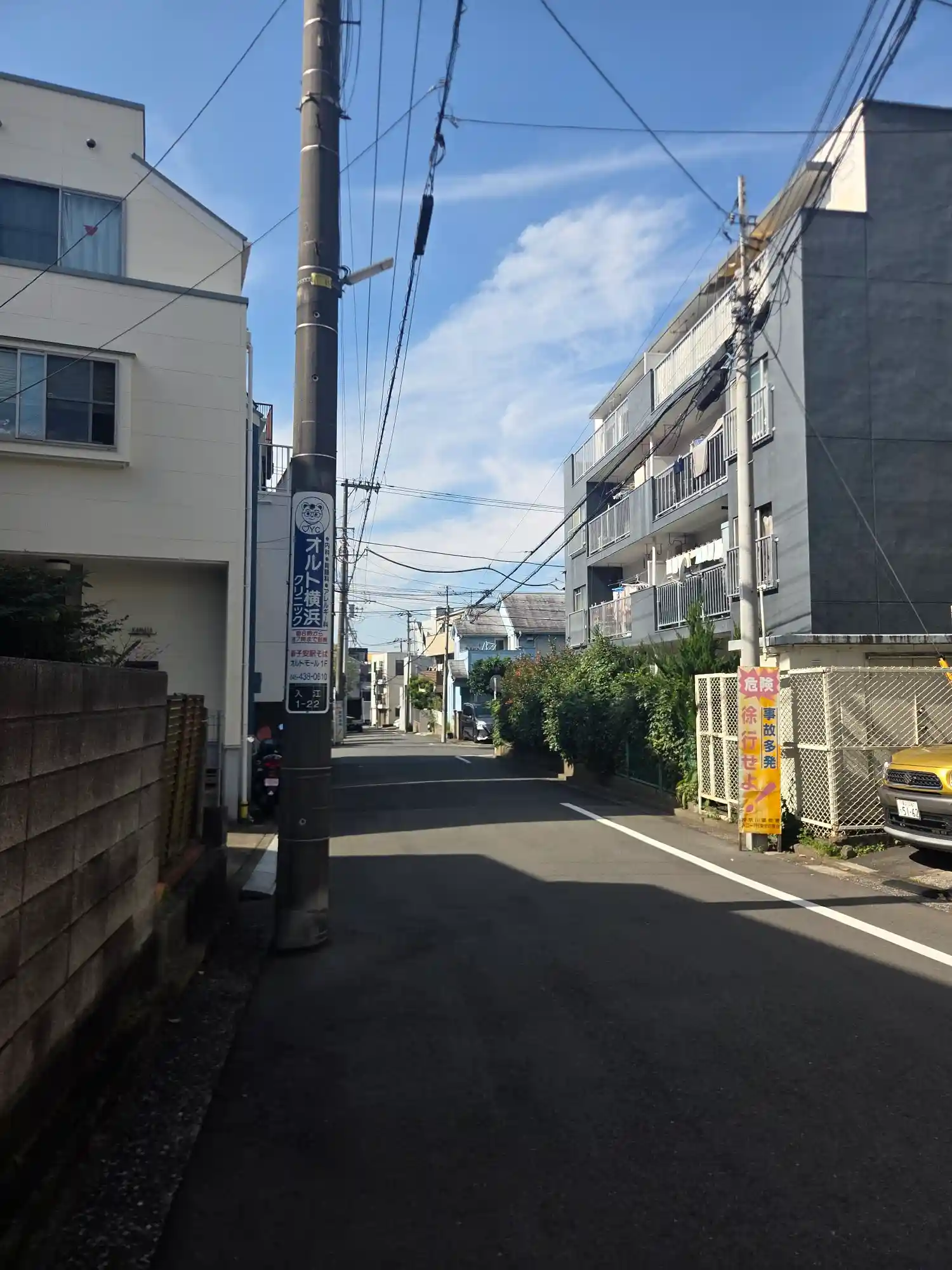 新子安駅から少し離れた住宅街の細い路地。中層の集合住宅と戸建てが並び、電柱には徐行を促す看板がある
