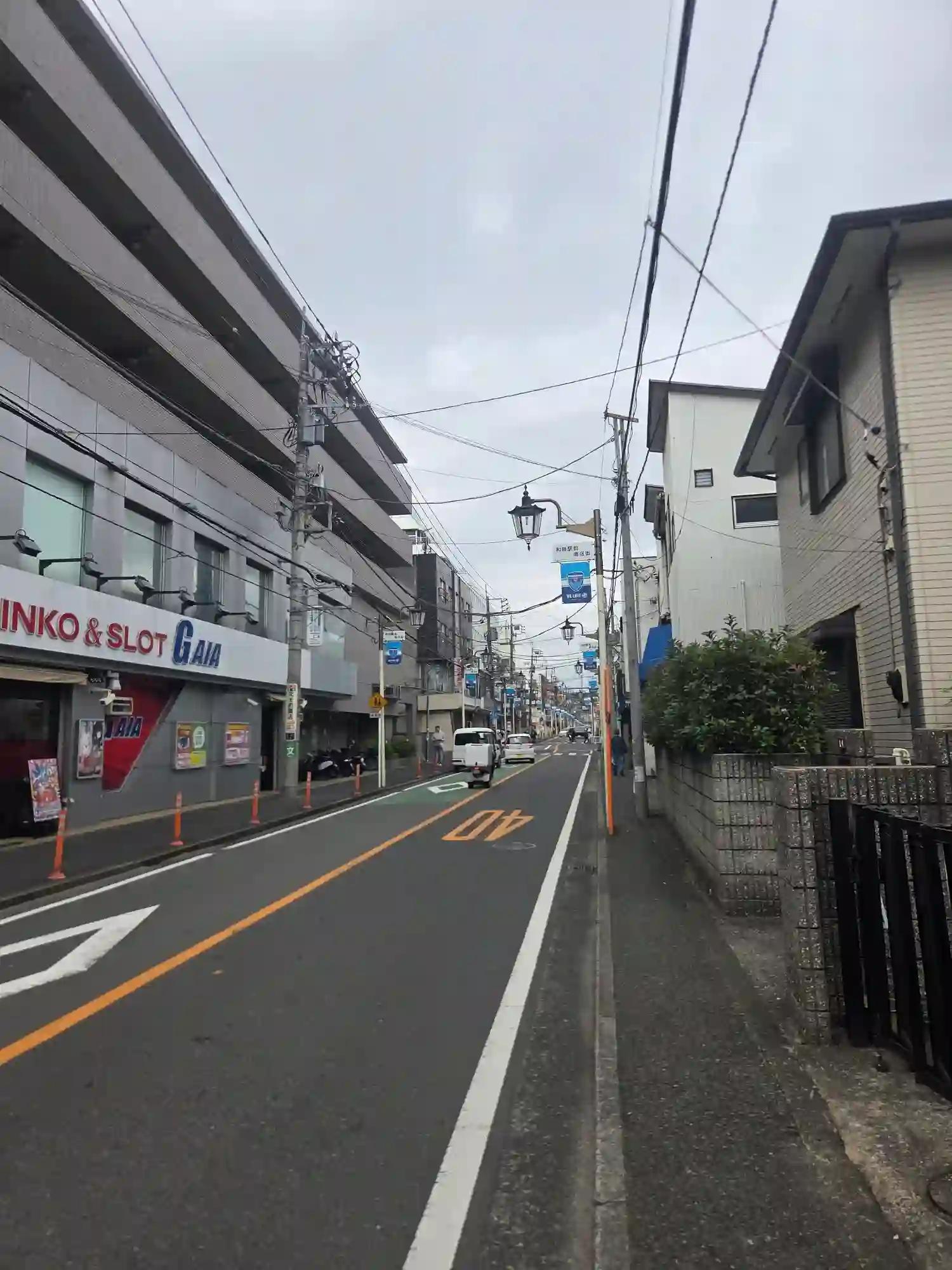 和田町駅前の通り。マンションや店舗、住宅が並び、街灯に商店街の旗が下がる。昼間は人通りが少なく落ち着いている